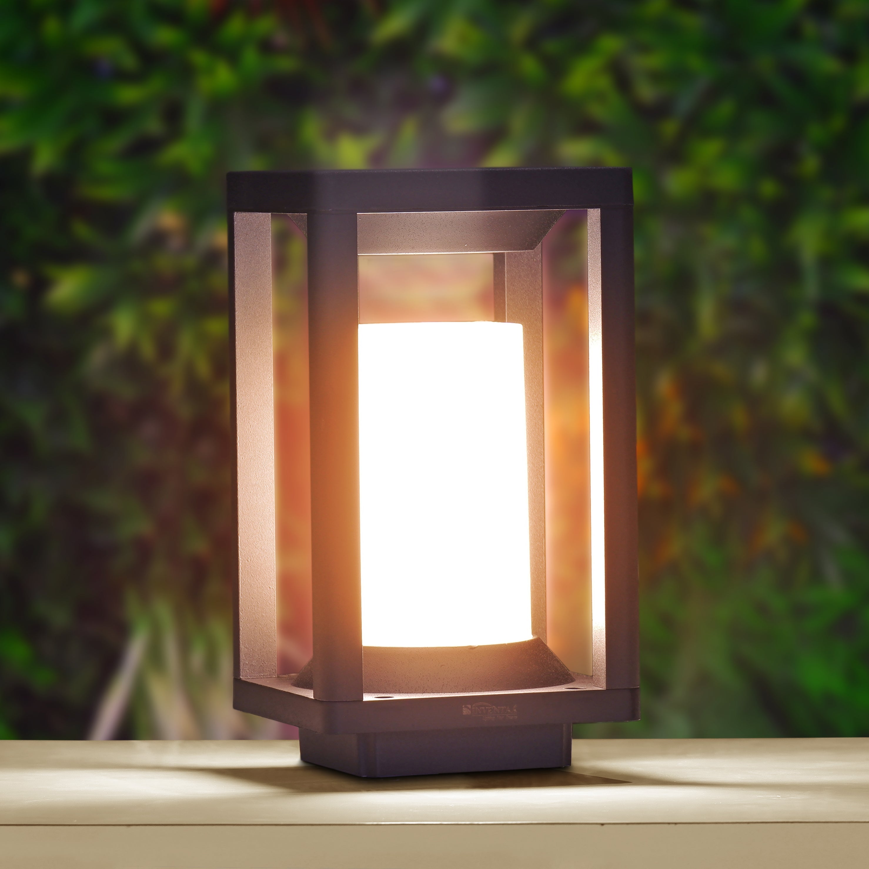 Outdoor lamp with a warm glow on a wooden surface against a blurred green foliage background